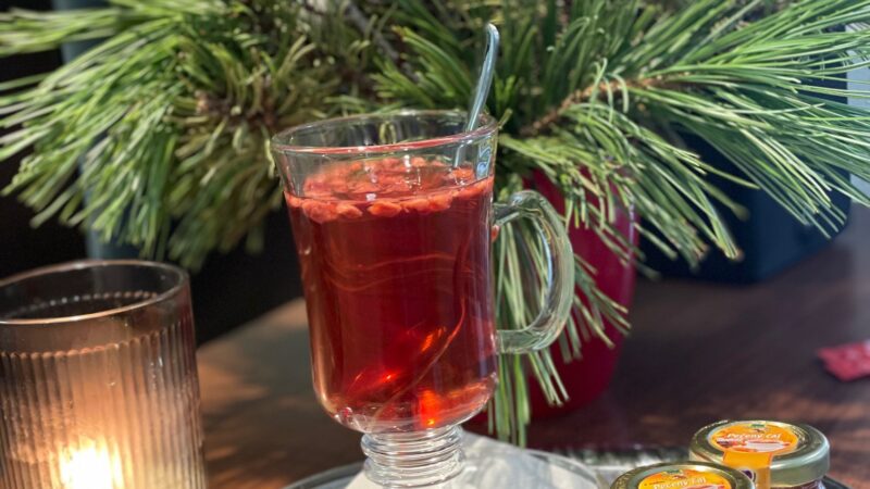 Pečený čaj v pohári obklopený vianočnou dekoráciou a vzorkami rôznych druhov pečeného čaju.