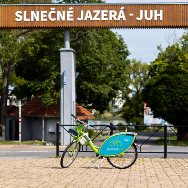 Zdieľaný bicykel pod tabuľou Slnečné jazerá, v pozadí je park.
