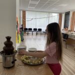 Čokoládová fontána s banánmi. Deti si máčajú nakrájané banány v čokoláde.