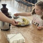 Čokoládová fontána s banánmi. Deti si máčajú nakrájané banány v čokoláde.