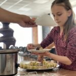 Čokoládová fontána s banánmi. Deti si máčajú nakrájané banány v čokoláde.